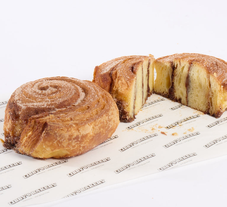 Two gluten free cinnamon buns with one slice cut in half on white background